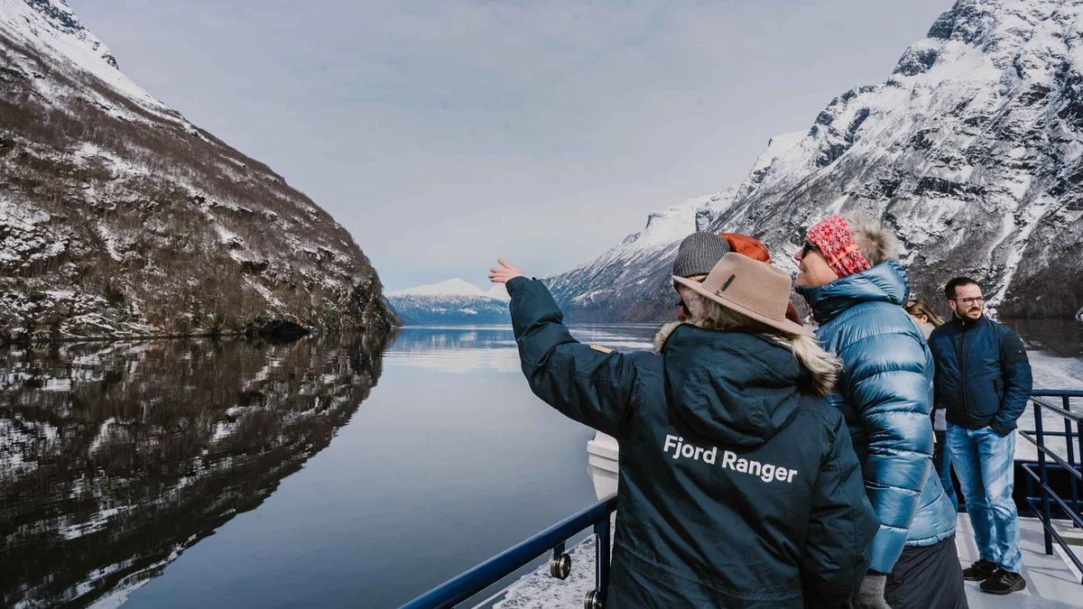 Snow-covered mountains above dark water on a winter Geiranger fjord cruise from Ålesund, Norway